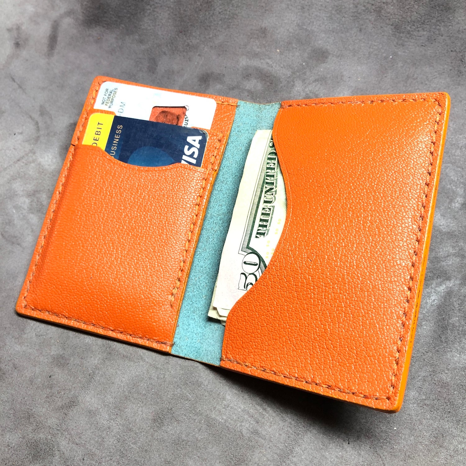 Orange leather wallet with cards and money on a gray surface. EPI leather luxury wallet, card case with goatskin leather lining, hand stitched, finished edges. 