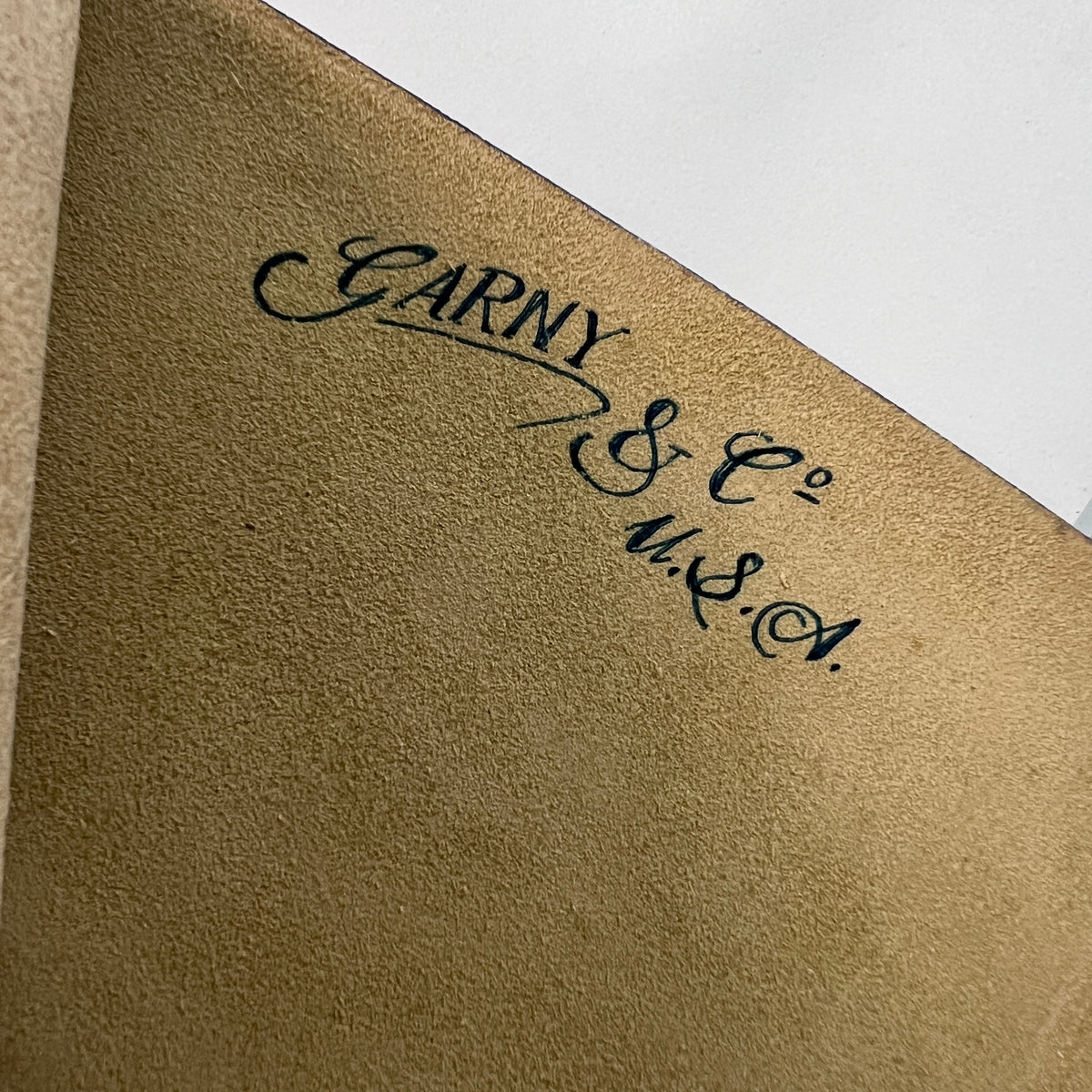 Close-up of a textured tan leather or suede surface with black cursive script reading 'Carny & Co. Made in USA.