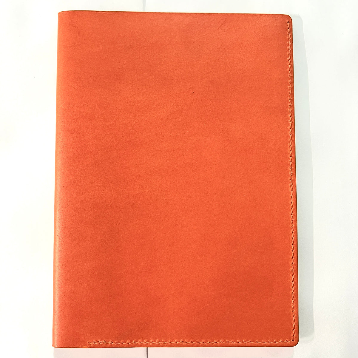 A bright orange cowhide  leather notebook cover or passport holder with visible hand stitching on a plain white background.