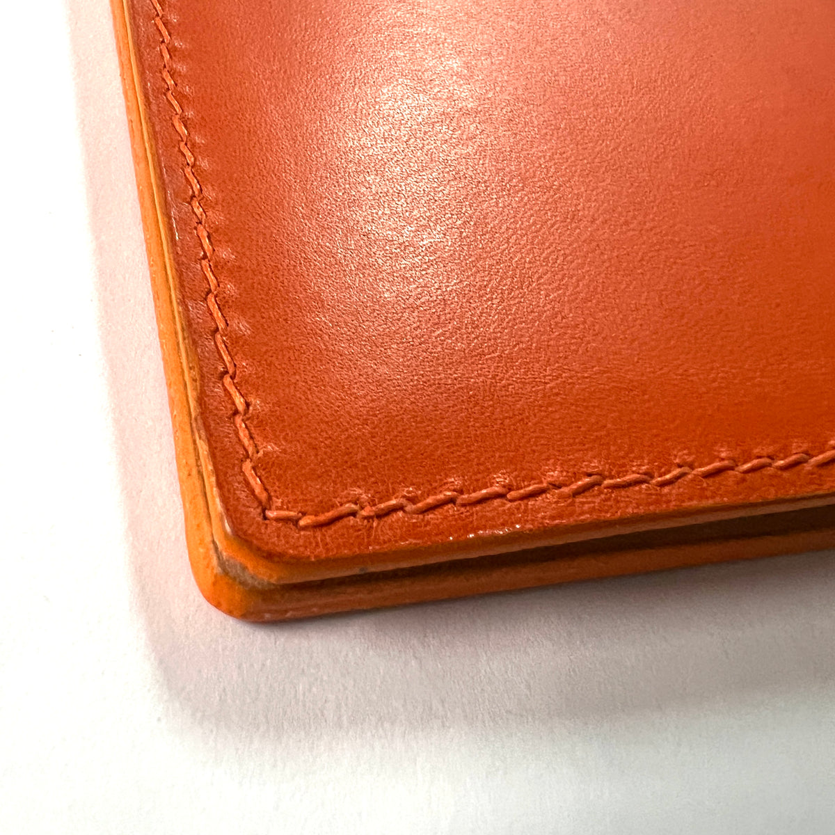 Close-up of a warm orange-brown leather journal corner with visible stitching, nicely finished edge, photographed on a white background.