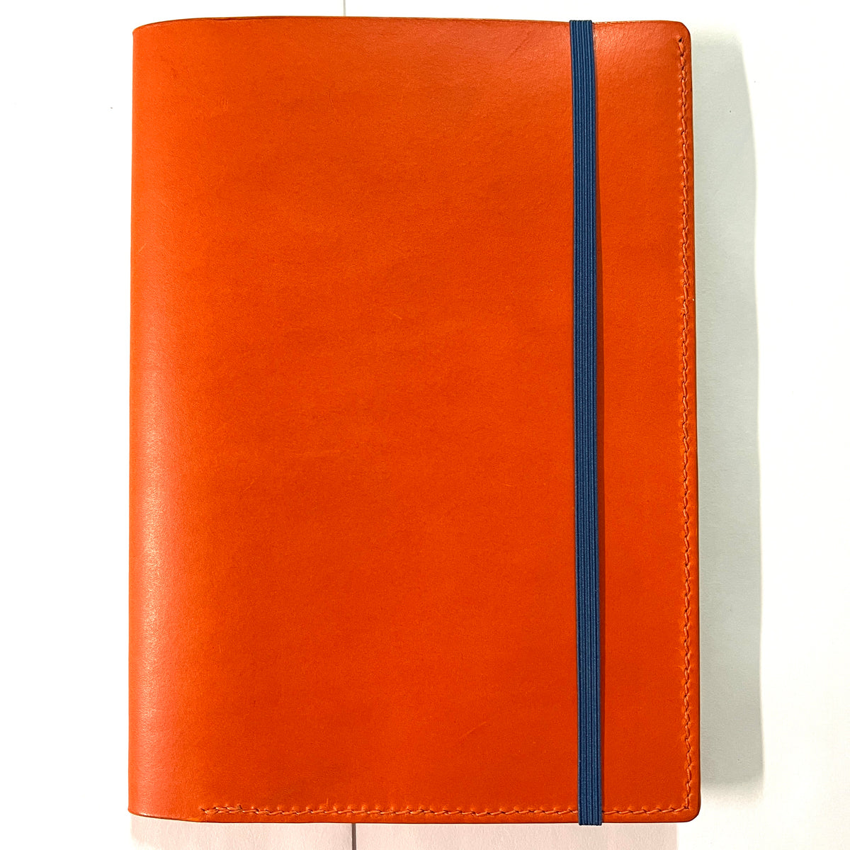 An orange leather notebook or planner cover with a vertical blue elastic closure band, shown flat against a white background.