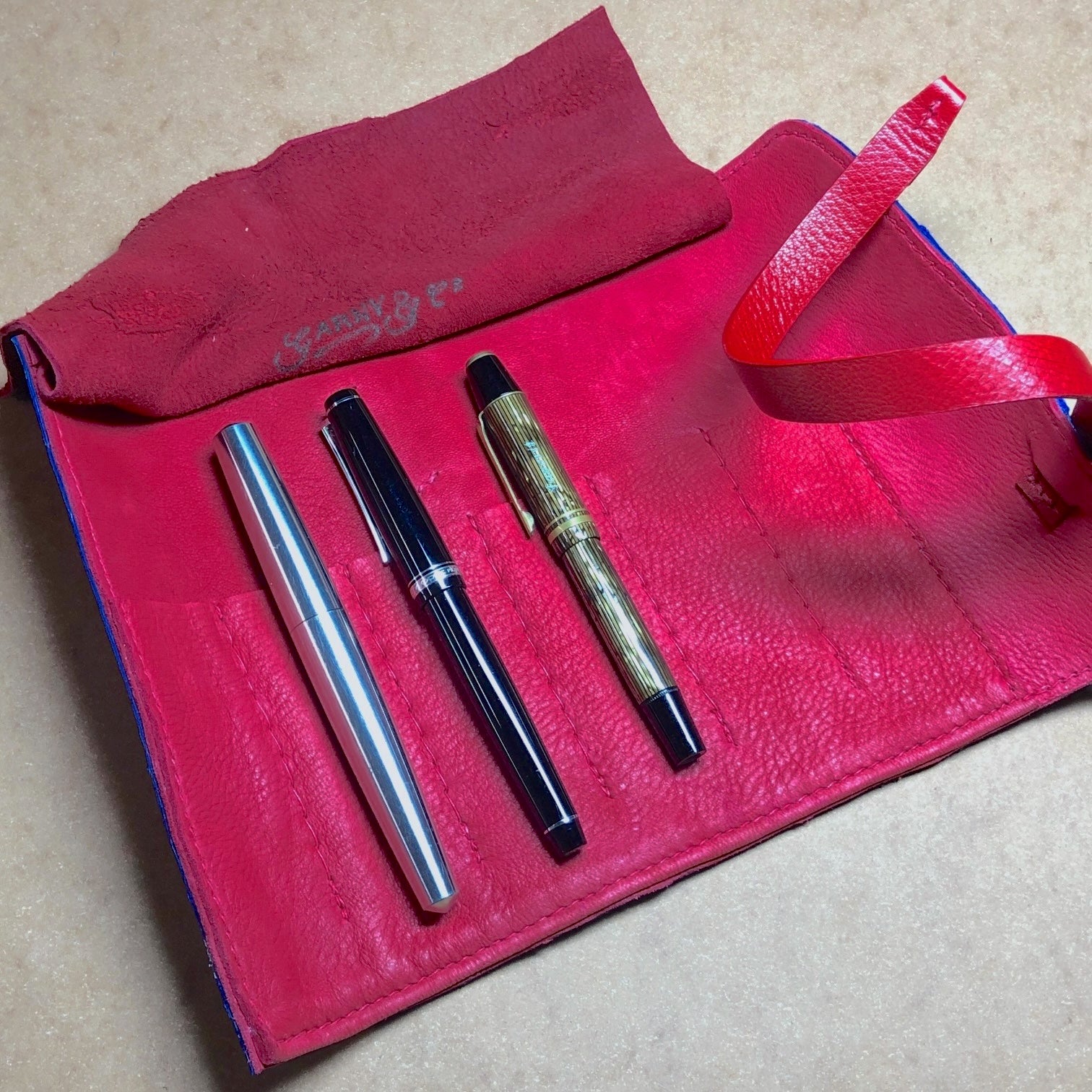 Three fountain pens on a red deerskin leather case, pen roll, inside. 