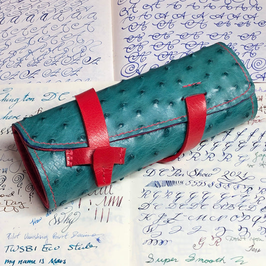 Teal pen roll, pen wrap with red strap closure, on a background with cursive text