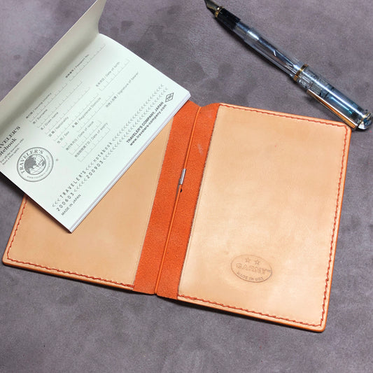 Cowhide leather Passport size Travelers Journal cover.  Hand stitched, finished edges. One Midori Travelers Notebook Journal included.  Orange leather notebook with a fountain pen on a gray surface.