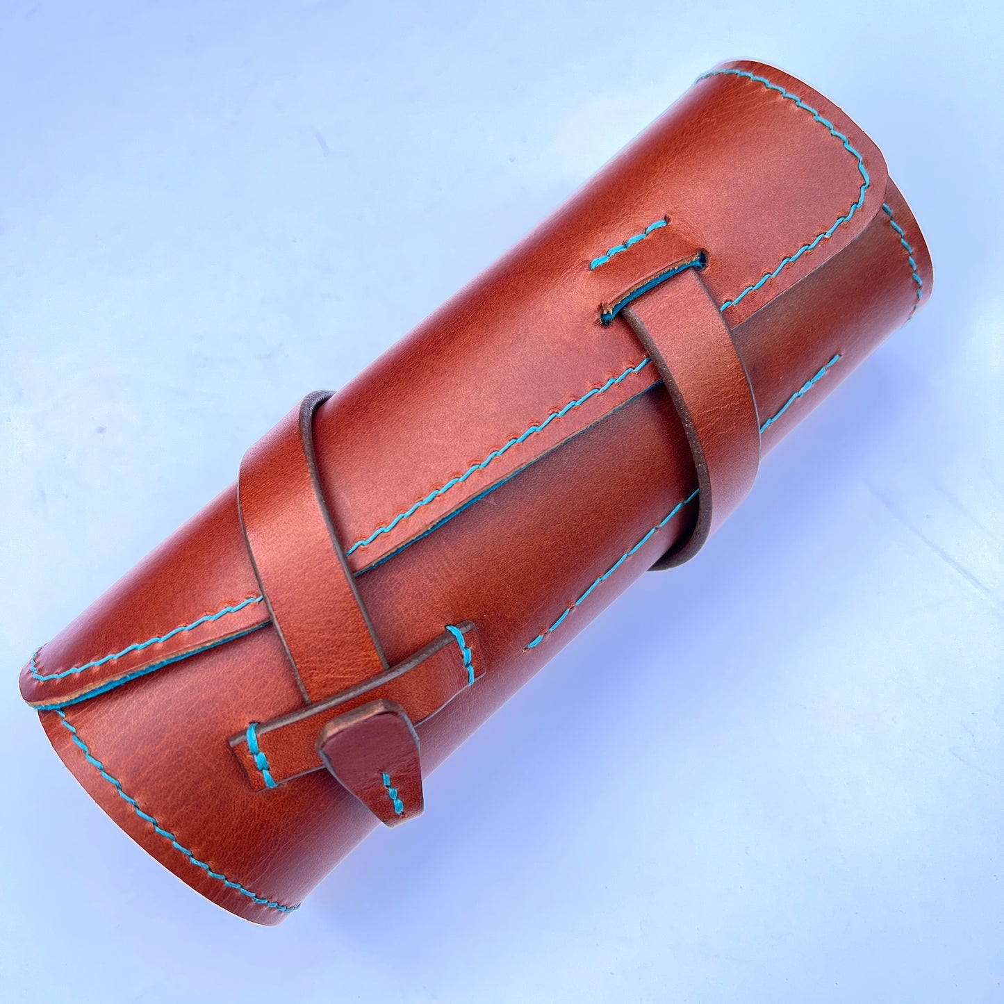 Brown leather roll with blue stitching on a light blue background