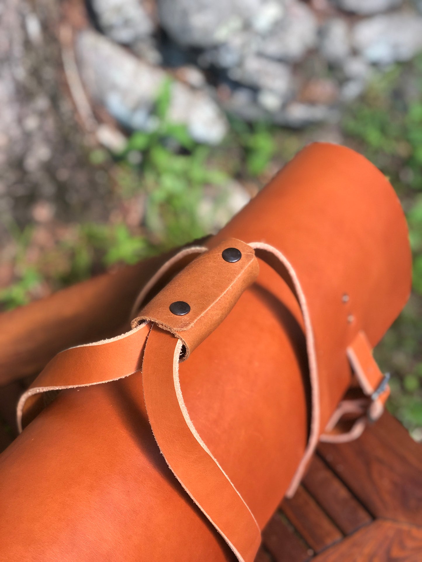Brown leather tool bag strap with rivets on a blurred natural background