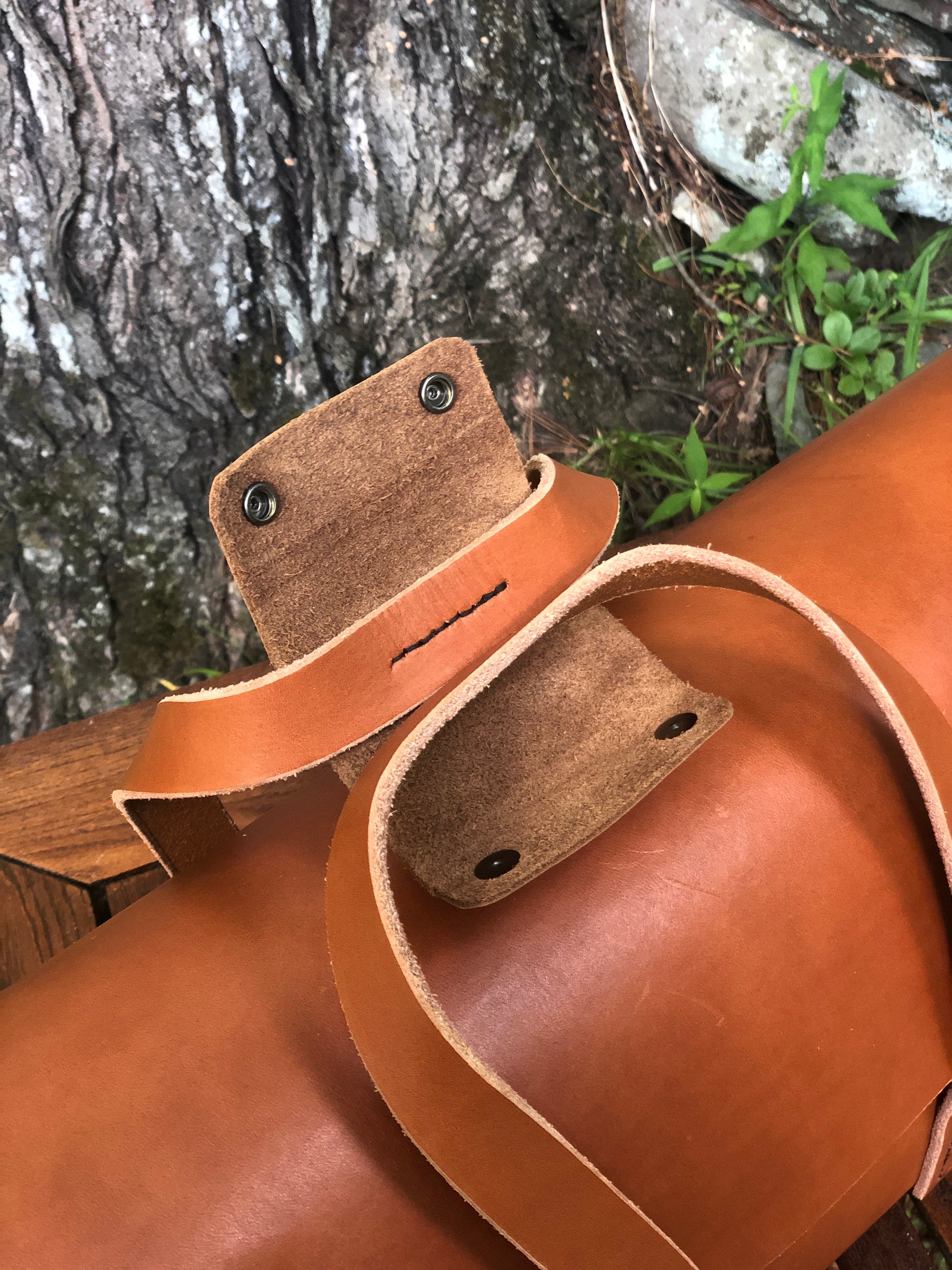 Close-up of a brown leather tool bag handle closure with stitching details on a natural background