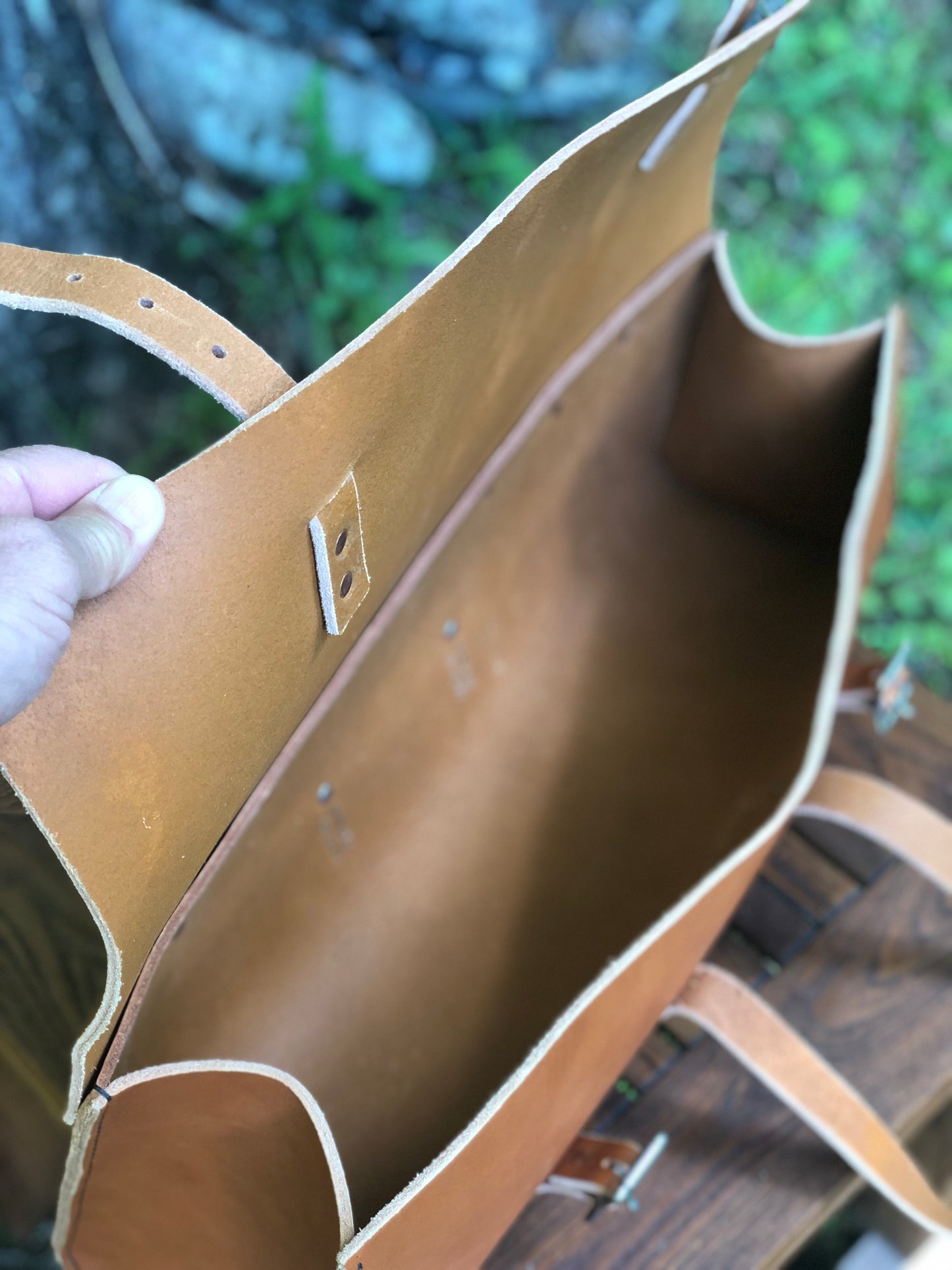 Inside of a brown leather tool bag with a visible brand logo held by a hand against a blurred natural background.