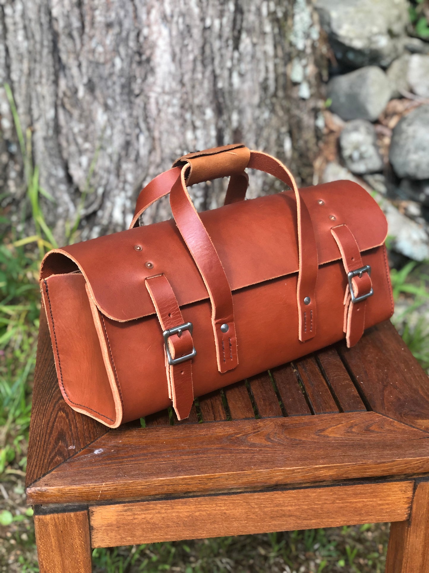 Brown leather tool bag on a wooden bench with a natural background