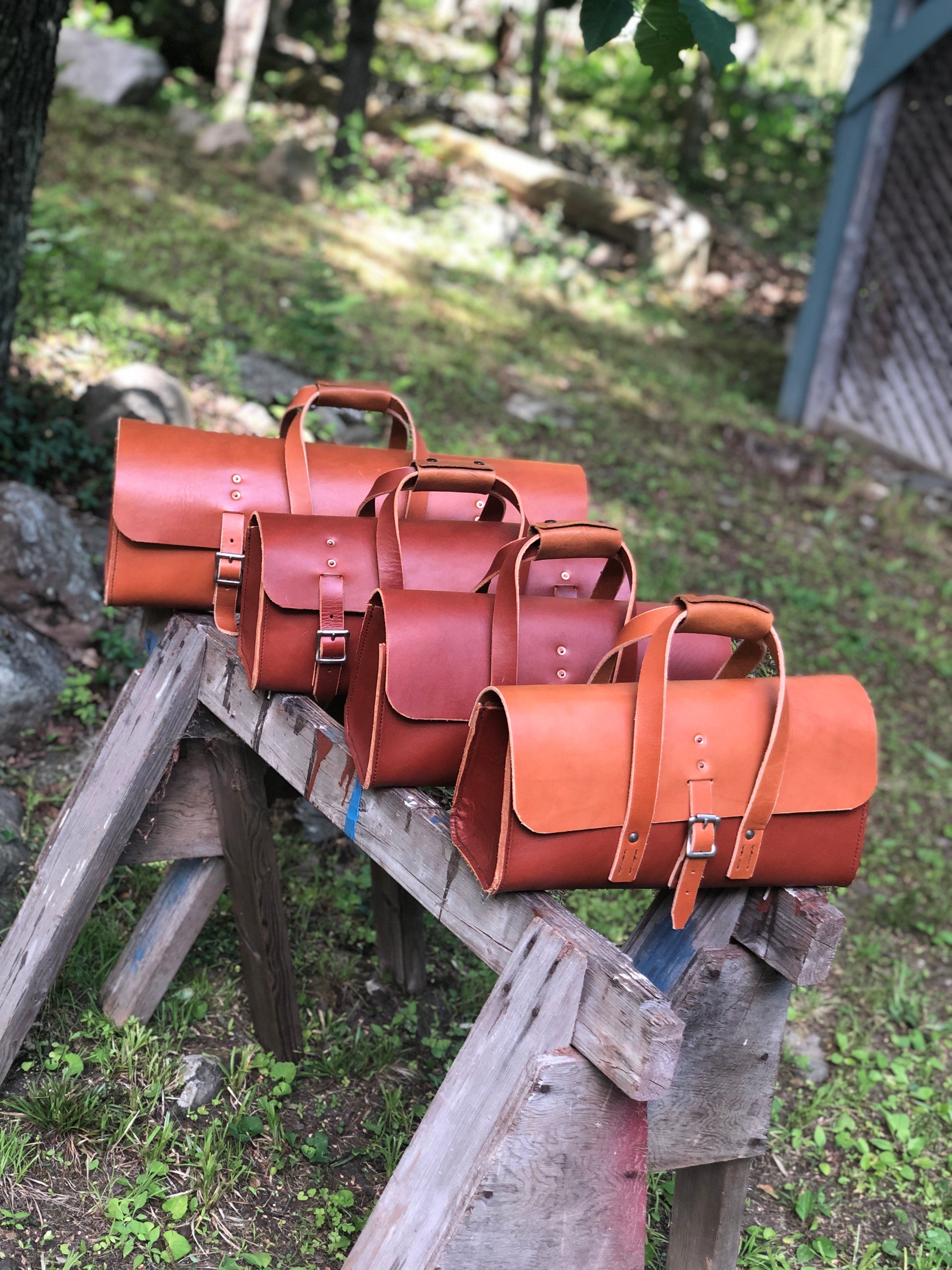 Set of brown leather tool bags on a wooden structure with a natural outdoor background