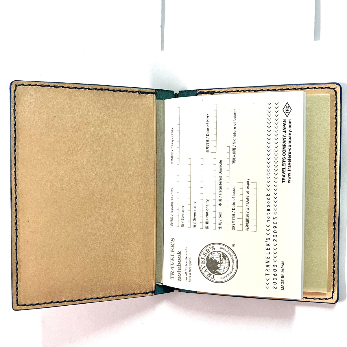 An open leather traveler's notebook with tan interior pages, dark green edging, and printed Japanese passport-style entry/exit sheets inside.