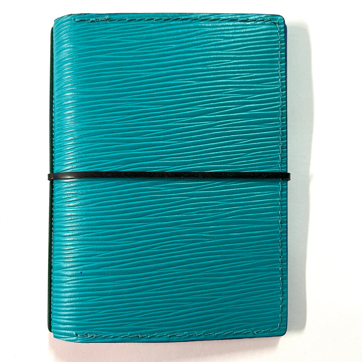 Cowhide leather Passport size Travelers Journal cover.  Hand stitched, finished edges. One Midori Travelers Notebook Journal included.  A teal blue textured leather notebook cover with a black elastic band closure, shown on a plain white background.